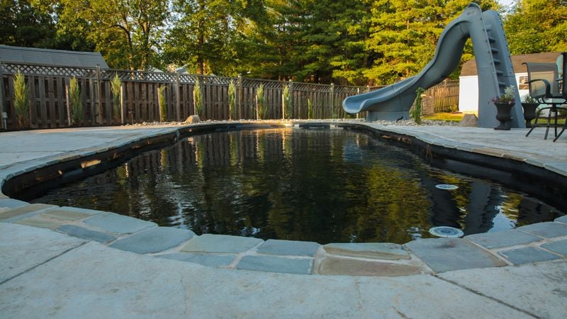 Black fiberglass pool with stone coping and pool slide