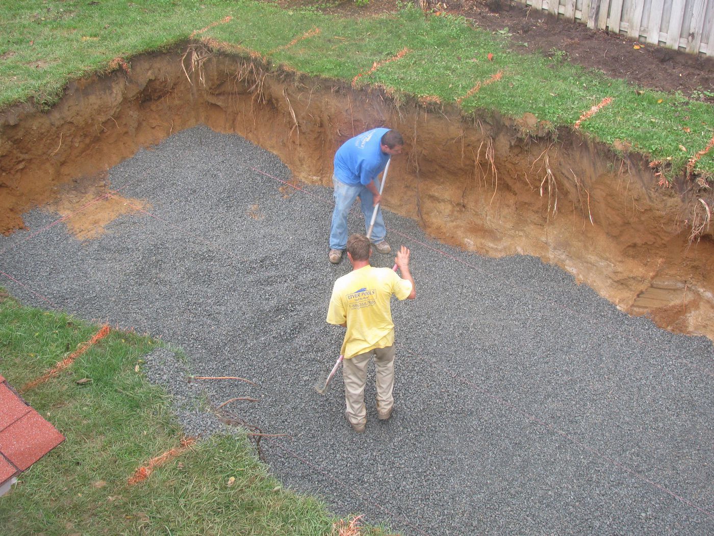 workers spread gravel in a pool foundation while preparing to install a fiberglass pool shell