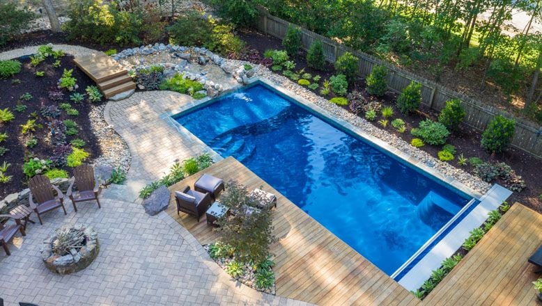blue fiberglass pool with landscaping and wood deck