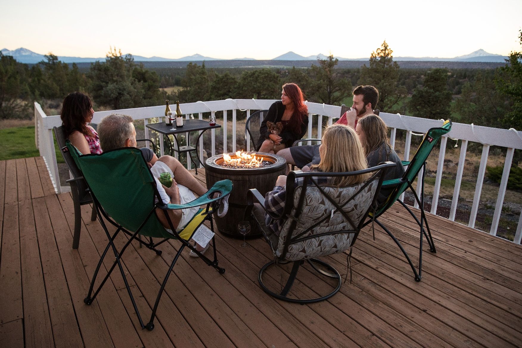 an outdoor gathering of several people around a circular fire pit on a backyard deck or patio